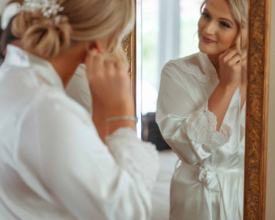 Bride putting on an earring in front of a gold-framed mirror